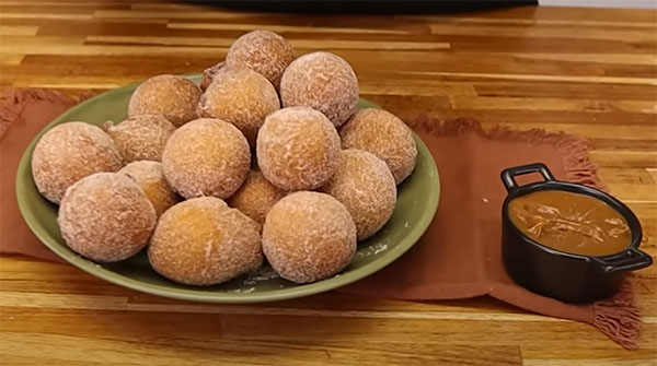 Bolinhos de chuva redondos, dourados e polvilhados com açúcar e canela num prato rústico