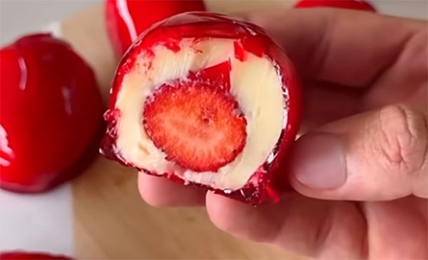 Corte de doce de morango inteiro envolvido com brigadeiro branco e cobertura vermelha